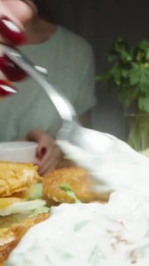 Dikey video. Beyaz soslu kadın, tavuk köftelerini burgerin üzerine sürer. Ev yemeği, akşam yemeği. Dolly kaydırıcı aşırı yakın çekim.