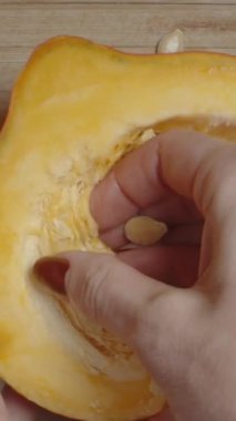 Dikey video. Kamera zumluyor, baştan aşağı bir yakın plan çekerken bir kadının eli balkabağından tohumları topluyor..