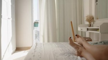 Güneşli bir sabahta parlak yatak odası. Kara Tırnak Cilalı Kadın Ayakları Yatakta Yatarken Parmaklarını Kıpırdatıyor. Rüzgâr Perdeleri Hışırdatır.