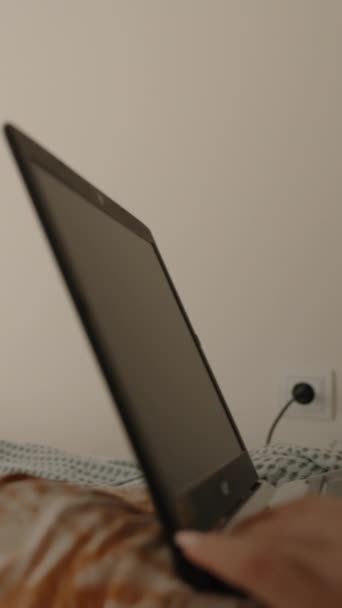 垂直录像 一位躺在床上的妇女正在笔记本电脑上工作 她的卧室明亮明亮 阳光照射在部分敞开的厚窗帘中 远程工作或学习 — 图库视频影像
