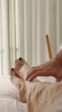Dikey video. Parlak ve güneşli yatak odası, bir erkeğin elleri tarafından okşanılan bir kadının birinci şahıs görüntüsü, yavaşça onları açığa çıkarıyor. Romantik İlişkiler kavramı.