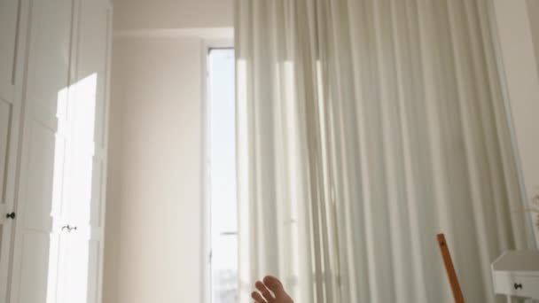 パノラマウィンドウから明るい日差しで照らされた白い部屋のトップダウンビューと カーテンを通るスライバー ベッドの上の男性の足のファーストパーソンビュー — ストック動画