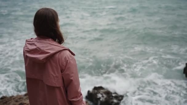 Одинокая Молодая Женщина Розовом Плаще Стоит Скалах Морском Шторме Глядя — стоковое видео