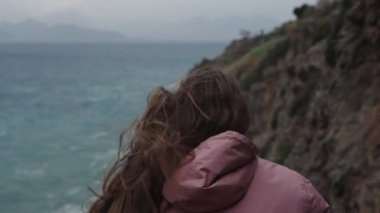 Yükseklerdeki Genç Bir Kadın, Denizdeki Fırtına, ve Güçlü Rüzgar Uzun Saçlarını ve Pembe Yağmurluğunu Kaldırıyor, Arkadan Görünüşü.