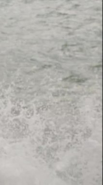Dikey video. Güçlü Rüzgarda Deniz kenarındaki Kayaların Arasında Pembe Kapüşonlu Yağmurluk Giyen ve Parmağıyla Bir Yeri Gösteren Bir Kadın.