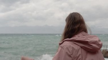 Denizde, Yüksek Dalgalardan Sıçrayan Fırtınada, Bir Kadın Pembe Yağmurluğunun Başlığını Giyer. Arka Görünüm, Yavaş Hareket.