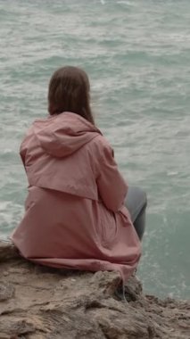 Dikey video. Yalnız Kadın Jagged Kayalıklarda Oturur ve Dalgaların Güçlü Dalgalarını Denizde İzler.