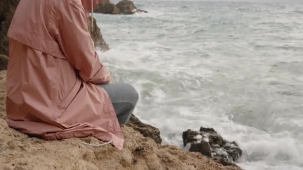 Samostatná Žena Růžové Bundě Kapucí Sedí Skále Zírá Zuřící Moře — Stock video