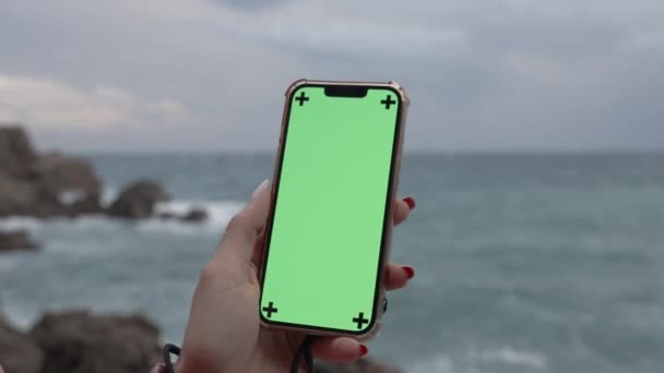 智能手机有一个铬键 绿色屏幕对一个热切和阴郁的季节斗篷 波浪冲击岩石的背景 — 图库视频影像