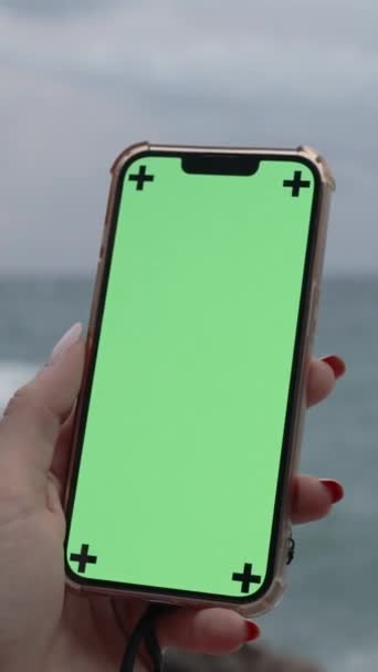 垂直录像 智能手机有一个铬键 绿色屏幕对一个热切和阴郁的季节斗篷 波浪冲击岩石的背景 — 图库视频影像