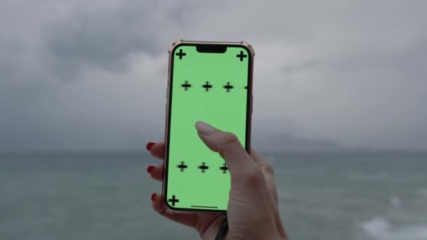 在海上阴雨天的背景下 手持绿色屏风的智能手机 手握追踪标志 侧身滑行 — 图库视频影像