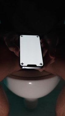 Dikey video. Karanlıkta, bir adam tuvalette oturur ve Beyaz Ekran ve Kameraya İzleme İşaretleri 'nin yakın plan planıyla akıllı bir telefon gösterir. Resminizi Eklemek için Beyaz Ekranı kullanın.