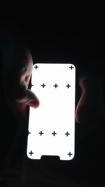 垂直录像 黑暗中卫生间里一个男人的头像 翻阅着智能手机屏幕 里面有一个空的白色空间供插入 他站起来 放在小木屋上 然后离开 — 图库视频影像