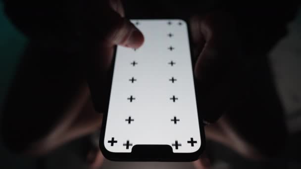 白い画面のレイアウトと暗闇のトイレに座っている男によってスクロールされている追跡マークを持つスマートフォンのクローズアップ — ストック動画