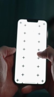 Dikey video. Loş Işıktaki Evlilik Odası, Kadın Çalışırken Erkek Telefonla Kaydediyor. Telefonda Beyaz Ekran Düzeni ve İzleme İşaretleri var. POV.