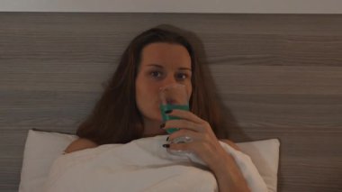 Yatakta genç bir kadının portresi, Kokteyl yudumluyor ve akşam geç saatte televizyon seyrediyor..