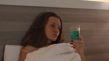 Genç bir kadının Cocktail yudumlarken, yatakta yorganın altında yatarken, yatmadan önce televizyon izlerken..