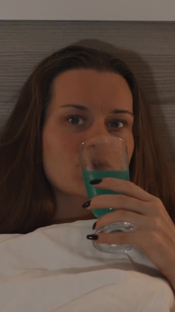 垂直录像 一个睡床的年轻女人的画像 喝着鸡尾酒 深夜看电视 — 图库视频影像