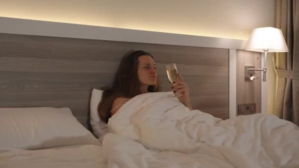 深夜时分 一位穿着睡裤 香槟和看电视的年轻女子 相机慢慢向后移动 明亮的卧室 — 图库视频影像