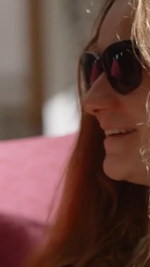 Dikey video. Güneş gözlüklü genç bir kadın Beyaz Kupa 'dan kahve içiyor ve gülümsüyor.