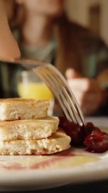 Dikey video. Kahvaltıda kirazlı krep. Çatalla birkaç böğürtlen zıpkınlayıp yerim. Yakın plan. Bir restoranda yemek yemek..