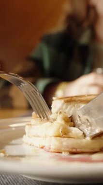 Dikey video. Tabağa bal serpiştirilmiş krep ve kiraz meyveleri. Bir parça kesip yiyorum. Bir kadınla restoranda kahvaltı, meyve suyu içiyor..