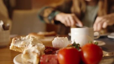 Bir kadınla bir restoranda kahvaltı. Krem peynirle ve tabakta yumurtalı domatesle kaplanmış rulo. Yakın plan..