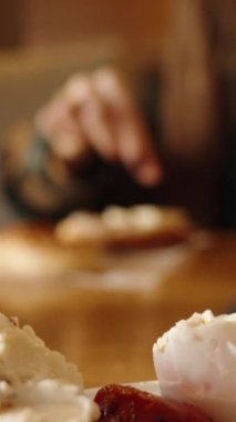 Dikey video. Restoranda kahvaltı, bir kadın kendine sandviç yapıyor, ekmeğin üzerine peynir ve jambon dilimleri koyuyor..