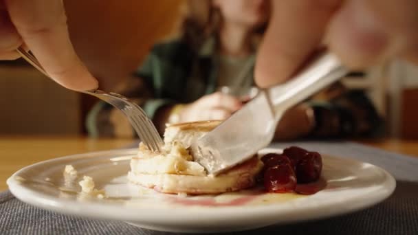 薄饼和樱桃浆果里撒满了蜂蜜在盘子里 我砍下一块吃了和一个女人一起在餐馆吃早餐 她在喝果汁 — 图库视频影像