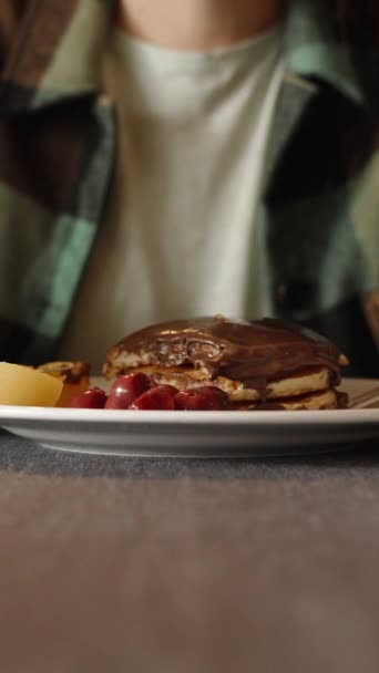 垂直录像 餐馆里的一位年轻妇女正在吃早饭 喝咖啡 盘子里有巧克力和水果煎饼 — 图库视频影像