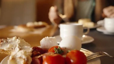 Bir kadın benimle restoranda kahvaltı yapıyor. Tabakta sosisli yumurta ve peynirli rulo var. Kahve masanın üstünde. Güzel, sıcak bir iç..