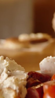 Dikey video. Bir kadın benimle restoranda kahvaltı yapıyor. Tabakta sosisli yumurta ve peynirli rulo var. Kahve masanın üstünde. Güzel, sıcak bir iç..