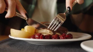 Çikolata, kiraz meyvesi ve şeftali kaplı bir tabağın yakın çekimi. Bir kadın bir parça keser ve yer. Restoranda kahvaltı..