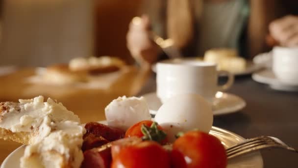 一个女人在餐馆里和我一起吃早餐 盘子里有鸡蛋和香肠 还有面包和奶酪 咖啡在桌子上 美丽温暖的内部 — 图库视频影像