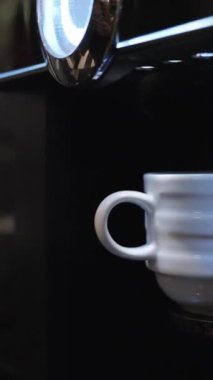 Dikey video. Kahve makinesi kahvenin hazır olduğunu göstermek için yanıp sönüyor ve bir adam fincanı alıyor. Yakın plan..