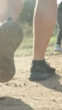 Dikey video. Ormanda Gezinti, Kameraya Parlayan Güneş Işıkları, Çimenlere ve Kuma Yürüyen Erkek Bacakları, İleride Bir Çocuk ve Kadın. Aile Tatili.