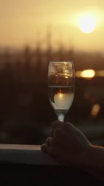 Dikey video. Balkondan Sunset 'in tadını çıkarırken elinde şampanya kadehiyle 