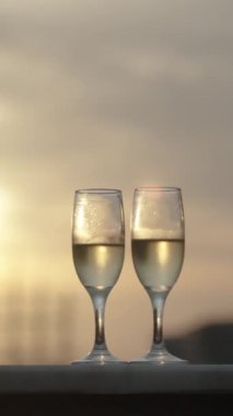 Dikey video. Dikey video. İki şampanya kadehi, romantik bir akşam, arka planda gün batımı, kamera dairesi. Gözlüklerdeki Güneş Yansıması.