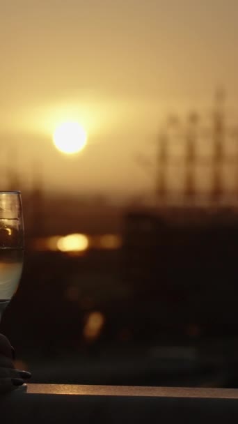 垂直录像 一个女人在高高的阳台上喝了一杯香槟 凝视着低矮的红色太阳和远方的船只 — 图库视频影像