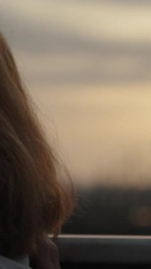 Dikey video. Dikey video. Uzun Saçlı Genç Bir Kadın Balkonda Duruyor, Şarabını yudumluyor ve Sunset ve Uzak Gemileri hayranlıkla seyrediyor.