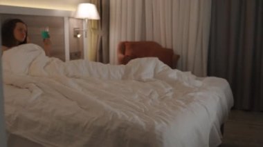 Kokteyl bardağıyla yatakta yatan ve televizyon izleyen genç bir kadının yatak odasına girmek. Akşam Romantik Atmosfer, Alkolizm Konsepti.