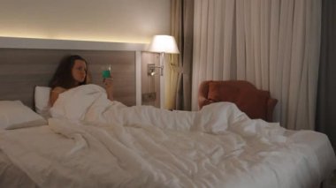 Akşamüstü, Yatakta Genç Bir Kadın Yeşil Kokteyl yudumluyor ve TV seyrediyor.