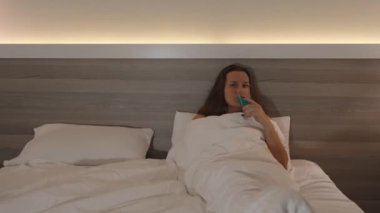 Yatakta Örtülerin Altında, Kokteyl İçen ve Akşam TV İzleyen Genç Bir Kadın. Panorama.