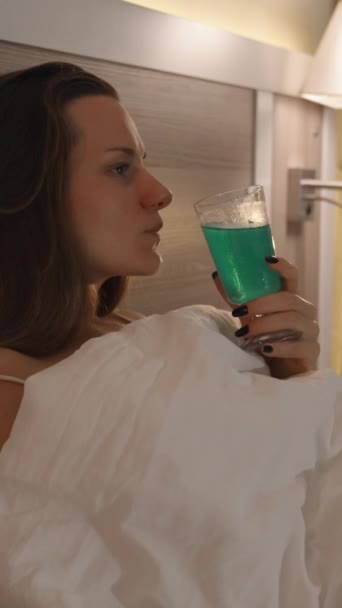 垂直录像 在床上的一个孤独浪漫的夜晚 灯光照亮了一个喝鸡尾酒的女人 慢动作 — 图库视频影像