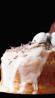 Dikey video. Siyah arka planda, beyaz kremalı bir pasta, bir çikolatalı kalp ve üzerinde küçük yumurtalar dönüyor. Paskalya Kutlaması.