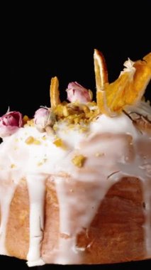 Dikey video. Üzerinde beyaz krema damlaları olan, üzerinde portakal dilimleri ve gül çiçekleri olan siyah arkaplanda pasta. Ev yapımı Paskalya pastası.