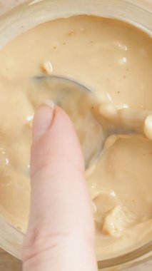 Dikey video. Kadın El Fıstık Ezmesini Parmağa Ayırır, Kaşığı Kavanoza Siler, Yakın plan.