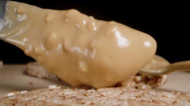 Siyah arka planda, pirinçli kekin üzerine bıçakla fıstık yağı yaymak, sağlıklı yemek. Dolly kaydırıcı, kapat..