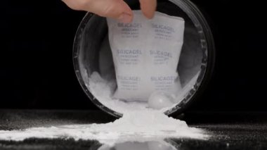 İçinde beyaz toz olan bir kavanozda paket, Emici Aşırı nem için silikon jel. Siyah bir Arkaplanda.