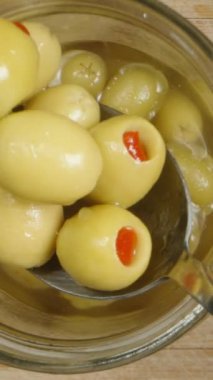 Dikey video. Bir kaşık kullanarak kavanozdan biberli bir avuç tuzlanmış zeytin alıp geri atıyorum. Üst görünüm, yavaş çekim.